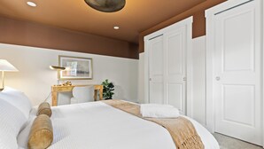 Ein Hotelzimmer mit Bett, Schreibtisch, Stuhl, Lampe, einem gerahmten Bild und einer Tür.