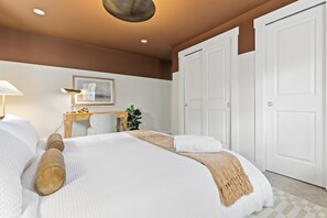 Ein Hotelzimmer mit Bett, Schreibtisch, Stuhl, Lampe, einem gerahmten Bild und einer Tür.