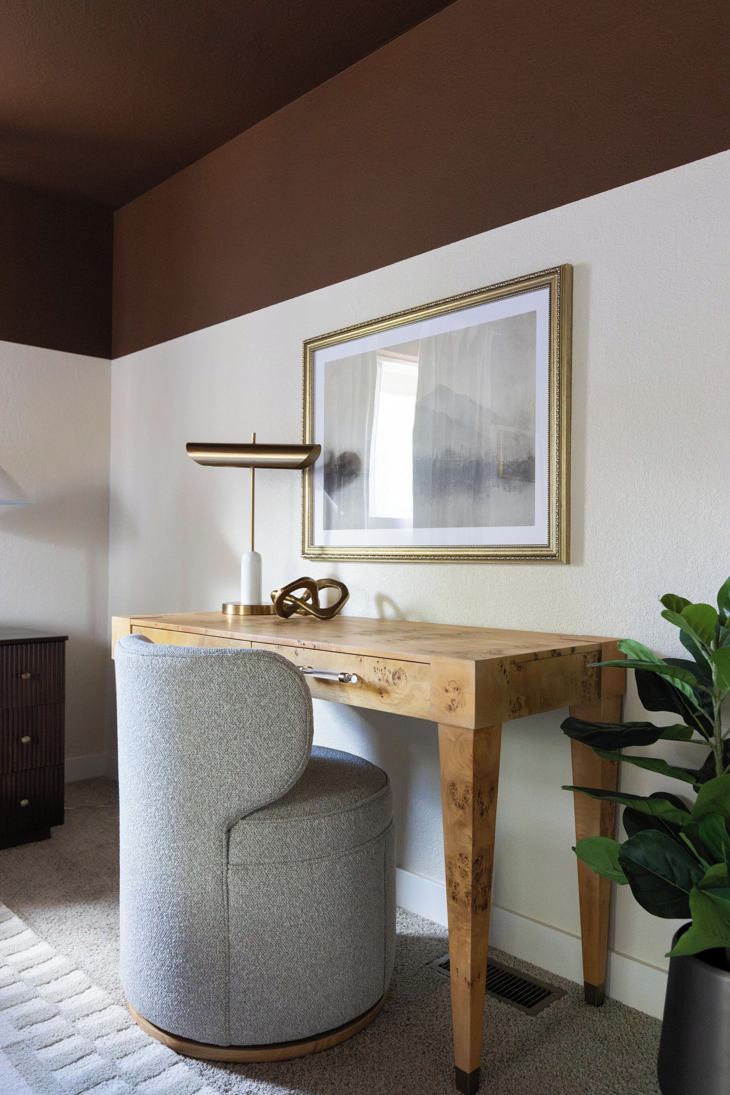 Un espace de bureau moderne avec un bureau en bois, un pouf rond, une lampe sur pied et un tableau encadré accroché au mur.