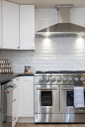 A modern kitchen with white cabinetry, a stainless steel range, and a built-in oven.
