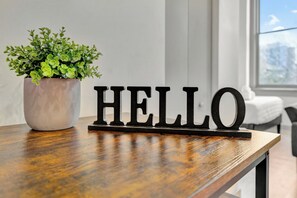 Une table en bois, sur laquelle se trouve un pot de fleurs et une pancarte noire avec le mot « HELLO ».