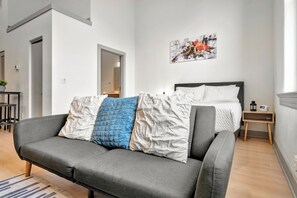 Un salon moderne avec un canapé gris, un lit avec une literie blanche et un tableau accroché au mur.