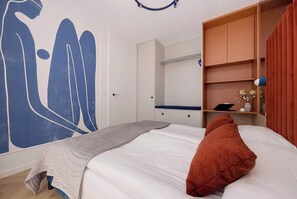 Une chambre à coucher comprenant un lit, une grande fresque murale, une armoire et un bureau avec un ordinateur portable.