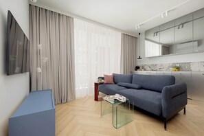 Un salon moderne avec un canapé gris, une table basse en verre et un téléviseur à écran plat fixé au mur.