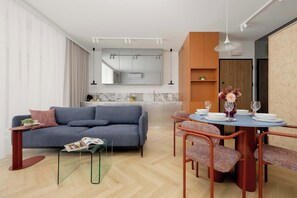 A modern living room with a grey sofa, a glass coffee table, and a dining area with a round table and patterned chairs. - Luxury Apartment in Chmielna Duo |Air Conditioning (Warszawa)