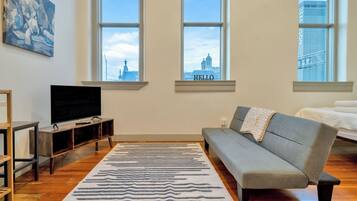 A living room with a television, sofa, and a large window with a view of a building.
