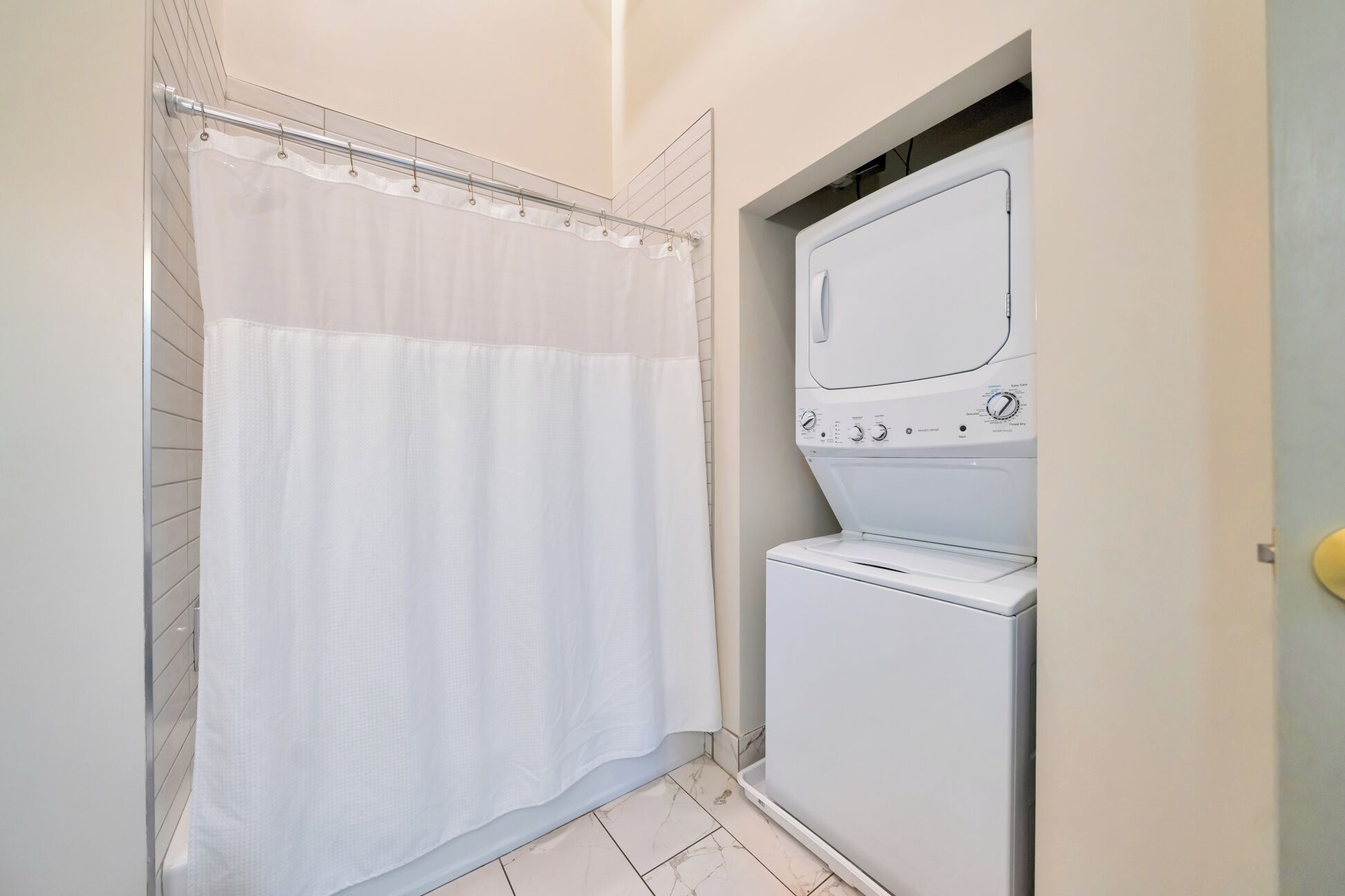 A small laundry room with a white washing machine and dryer, a shower curtain, and tiled flooring.
