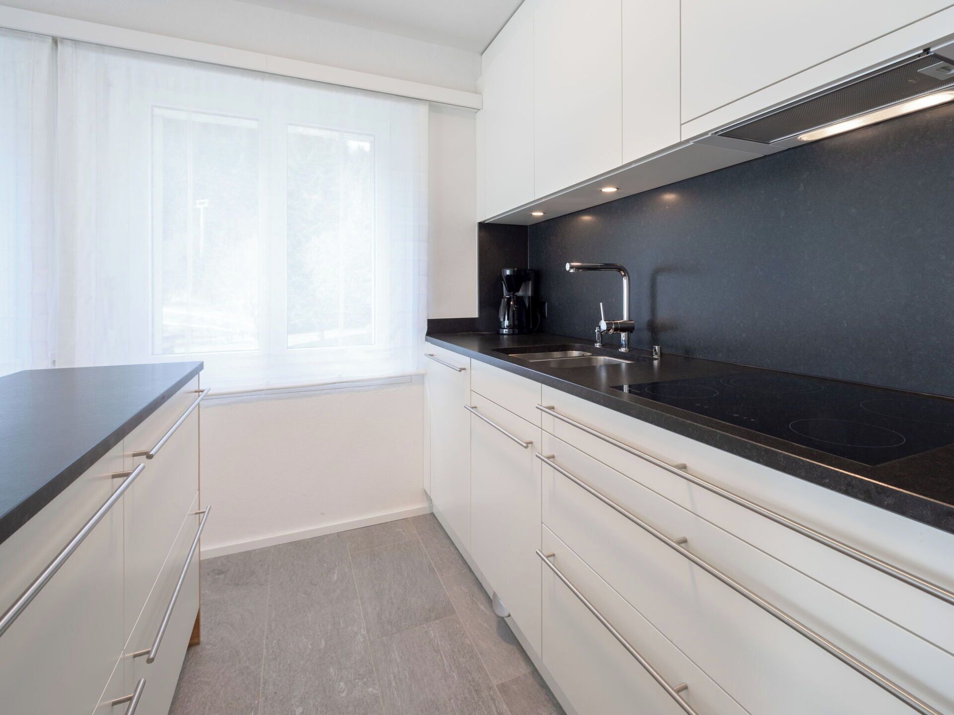 A modern kitchen with a black countertop, stainless steel sink, and white cabinetry.