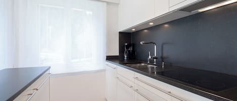 A modern kitchen with a black countertop, stainless steel sink, and white cabinetry.