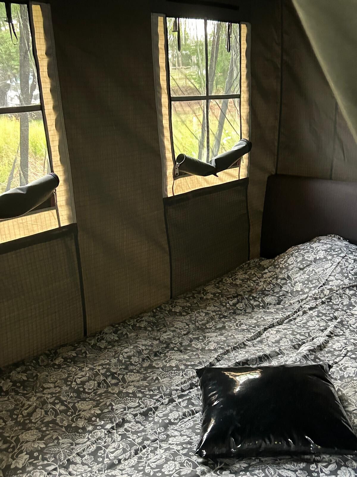 A tent-style room with a bed, a window with a view of trees, and a pillow on the bed.