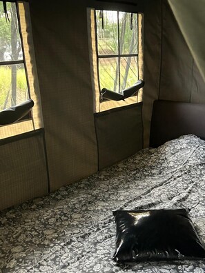 A tent-style room with a bed, a window with a view of trees, and a pillow on the bed. - Camping Pieterom - The Drenthe Safari (Sleen)