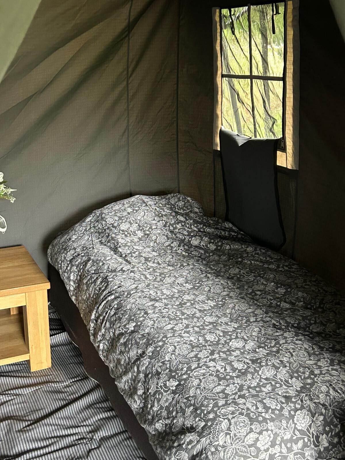 A single bed with a patterned bedspread in a tent-like room with a window.
