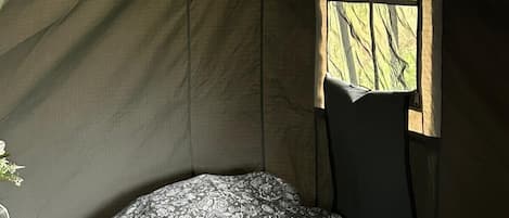 A single bed with a patterned bedspread in a tent-like room with a window.