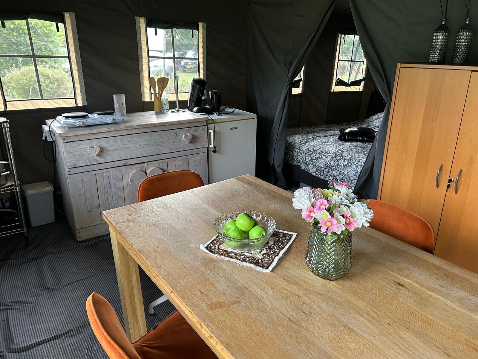 A tented accommodation with a dining table, chairs, a bed, and a wardrobe.