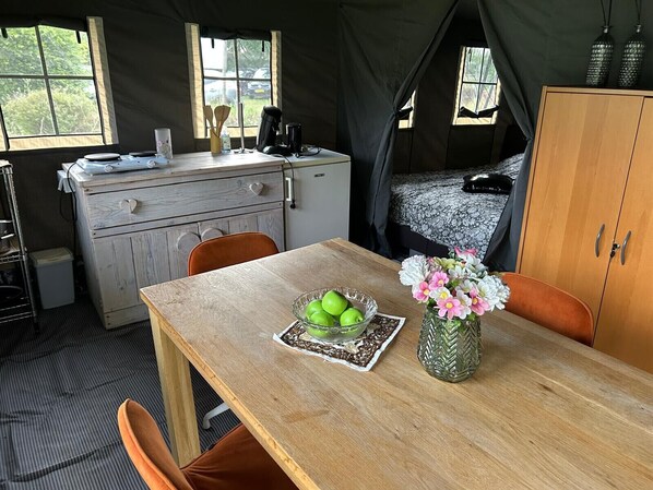 Alojamiento con carpa que incluye una mesa de comedor, sillas, una cama y un armario.