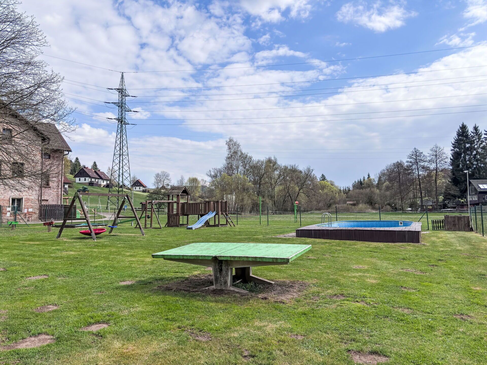 A grassy outdoor area with a swing set, a slide, and a small pool.