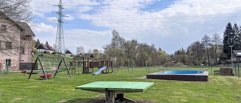 A grassy outdoor area with a swing set, a slide, and a small pool.