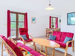 Ein Zimmer mit einer Sofagarnitur, einem Esstisch, Stühlen und einer Hängeleuchte.