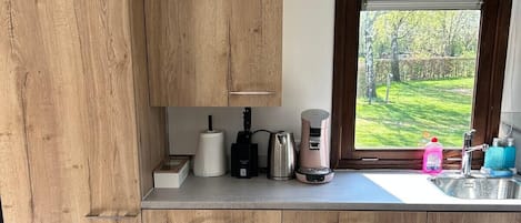 A kitchen with wooden cabinets, a countertop with various appliances, and a window with a view of greenery.