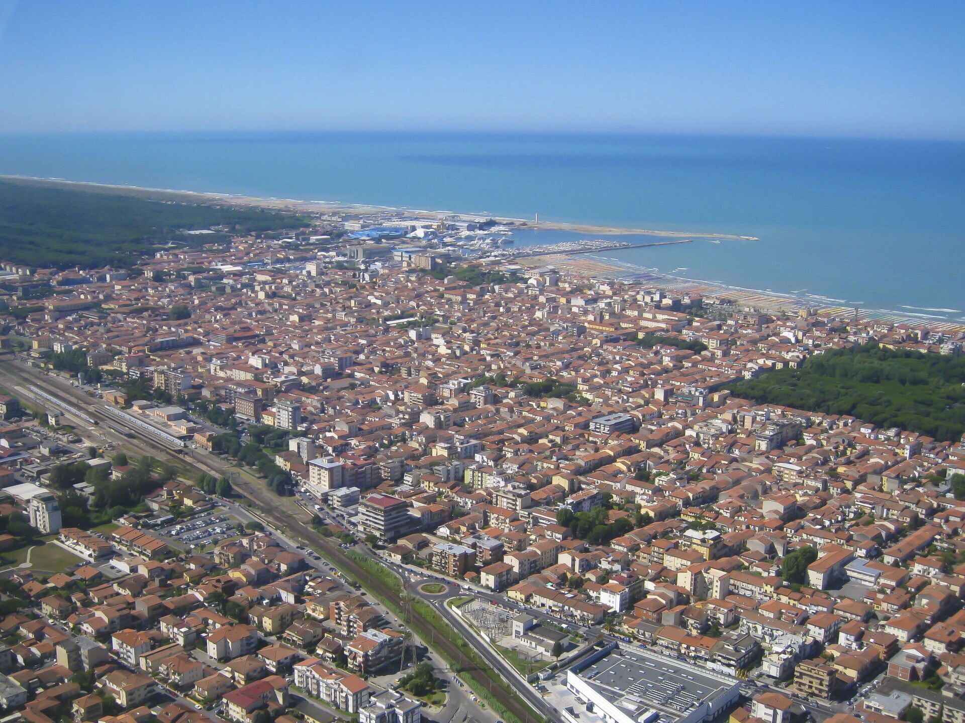 Eine Luftaufnahme einer Küstenstadt mit dichter Bebauung, einer markanten Bahnlinie und freiem Blick auf das Meer.