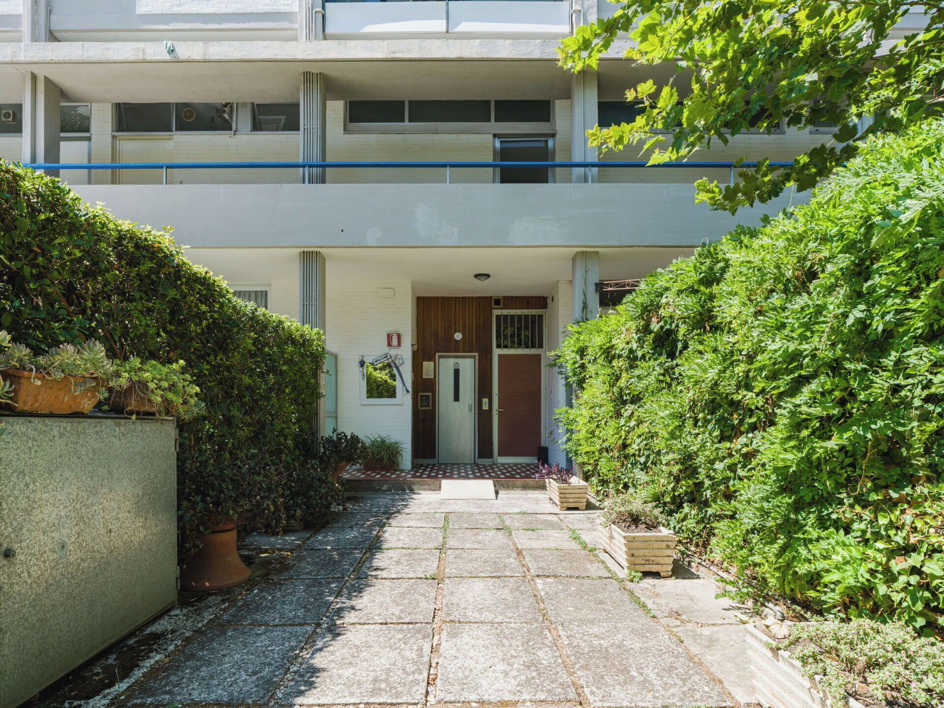 A two-story building with a central entrance, a small porch, and a pathway leading to the door.