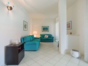 Un salon moderne avec deux canapés de couleur turquoise, un meuble en bois foncé et un sol carrelé de couleur blanche.