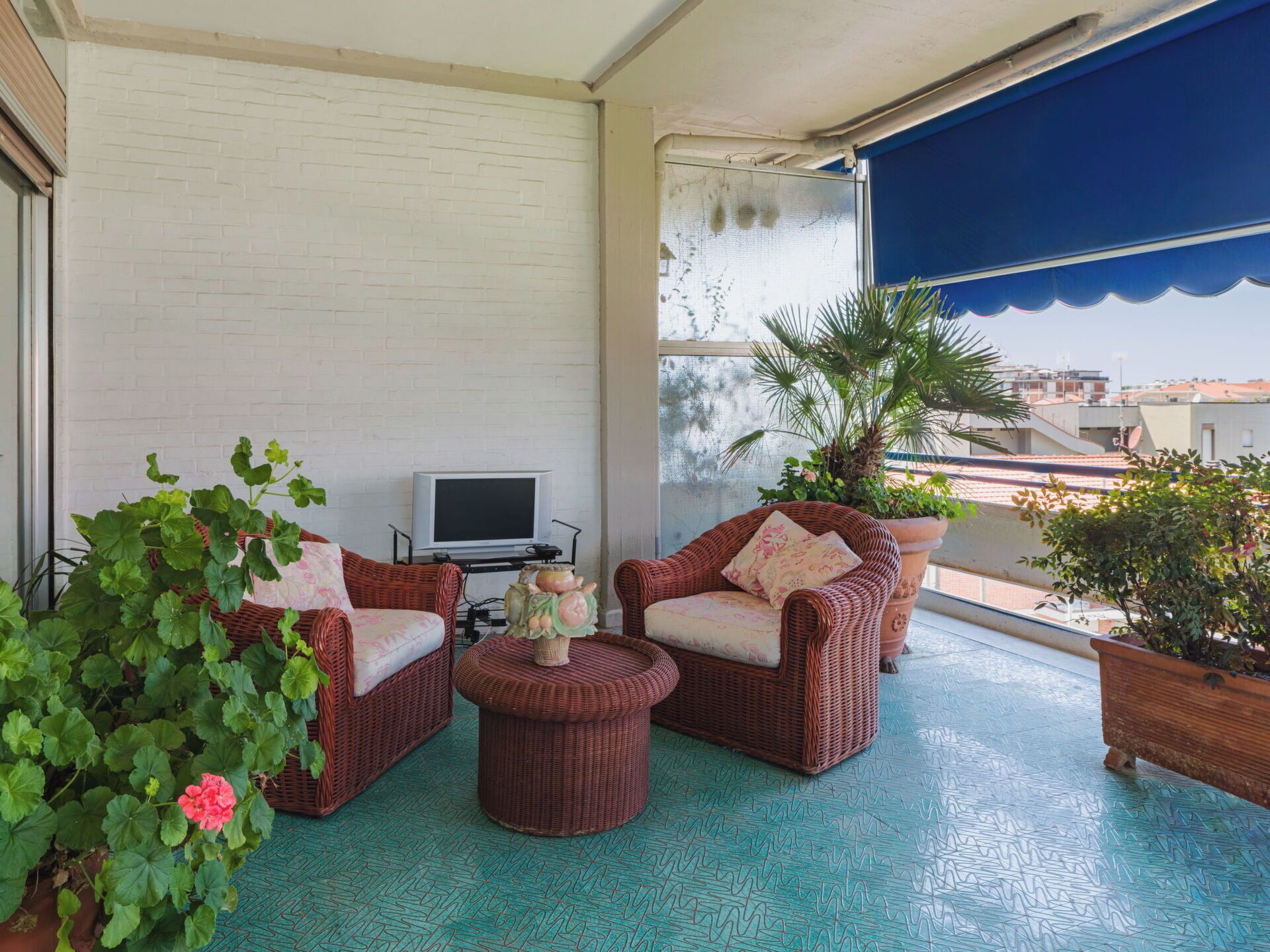 A balcony with wicker furniture, a television, and potted plants.