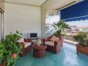 Un balcon agrémenté de meubles en osier, d’un téléviseur et de plantes en pot.