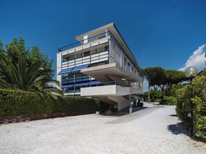 Ein modernes Mehrfamilienhaus mit Balkonen, einer Schotterauffahrt und umgebender Bepflanzung.
