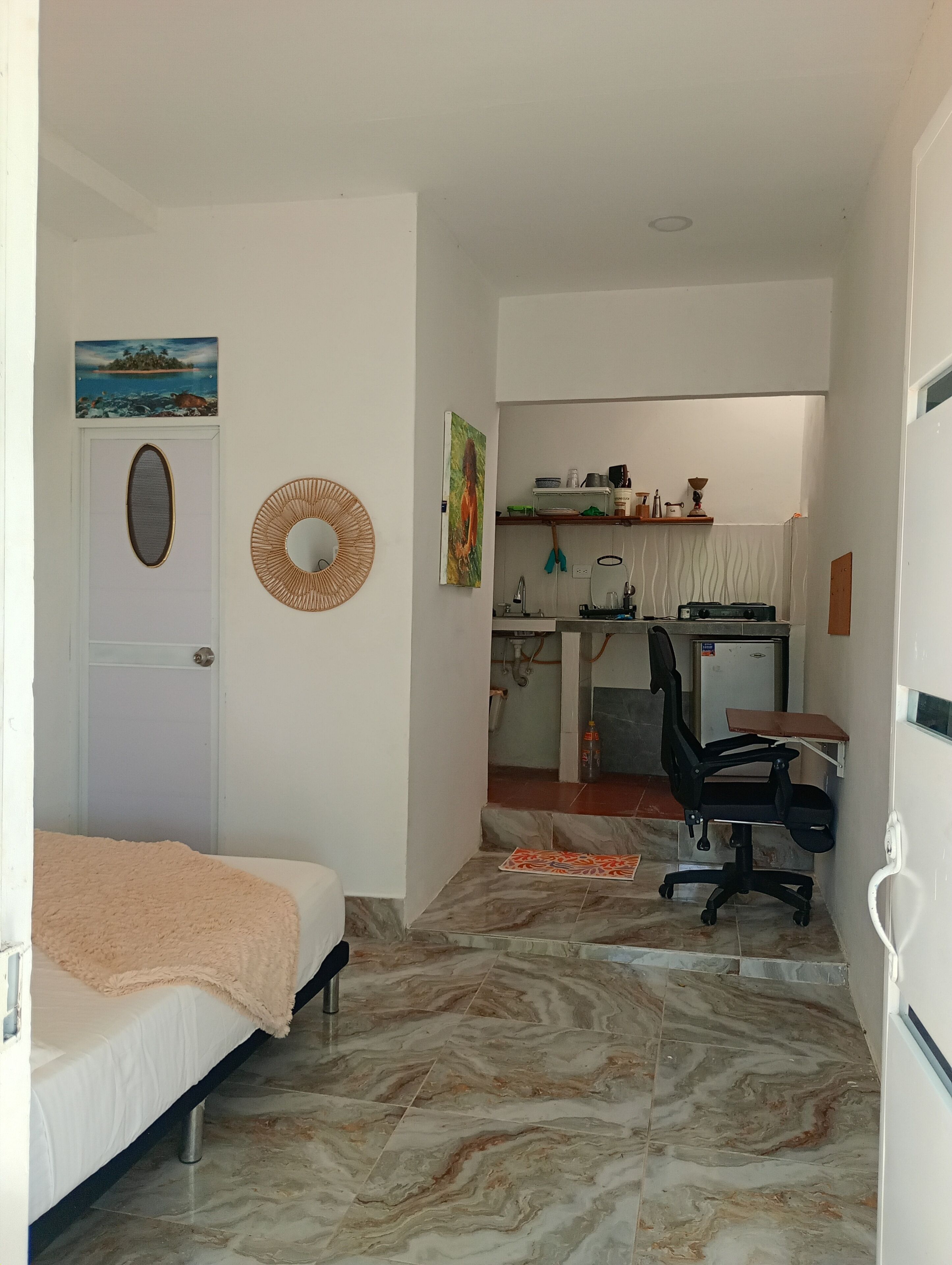 A bedroom with a bed, a desk with a chair, a small kitchen area, and a bathroom.
