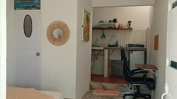 A bedroom with a bed, a desk with a chair, a small kitchen area, and a bathroom.