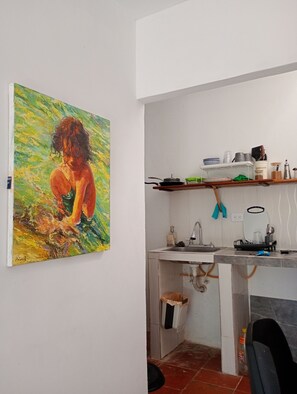 Una cocina con un lavamanos, encimera y un estante arriba. Hay un cuadro en la pared a la izquierda.