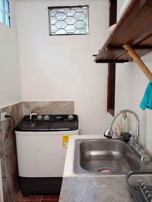 Cocina compacta con lavadora, un lavabo y una pequeña ventana de diseño hexagonal.