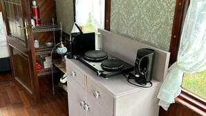 A compact kitchenette with a stove, a coffee maker, and a small shelf with kitchenware.