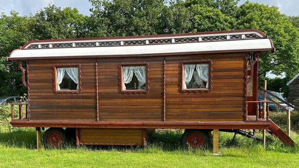 A stationary wooden house with a porch and two windows with curtains.