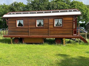 A stationary wooden house with a porch and two windows with curtains.
