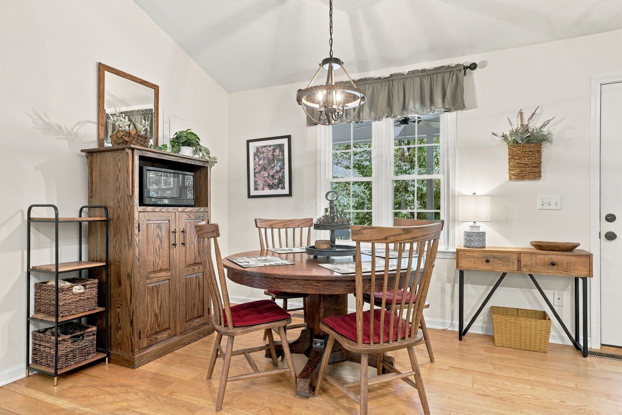 A dining area with a wooden table, chairs, a chandelier, and a view of greenery outside.