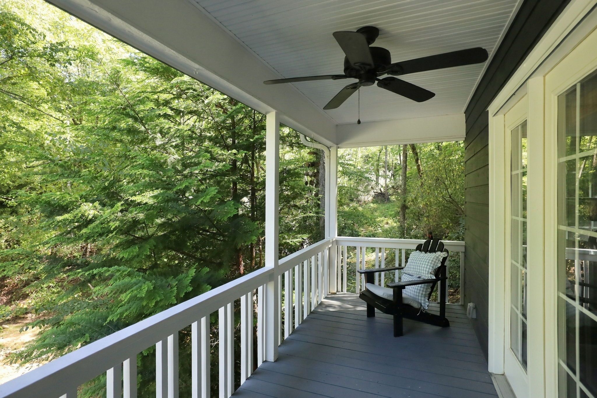 A covered porch with a ceiling fan, a bench, and a view of a forested area.