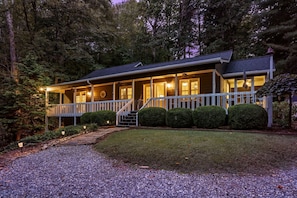 A two-story house with a porch, a staircase, and a well-maintained lawn. - Mountain Thyme-Ideal location: close, with privacy, forest stream & waterfall (Saluda)
