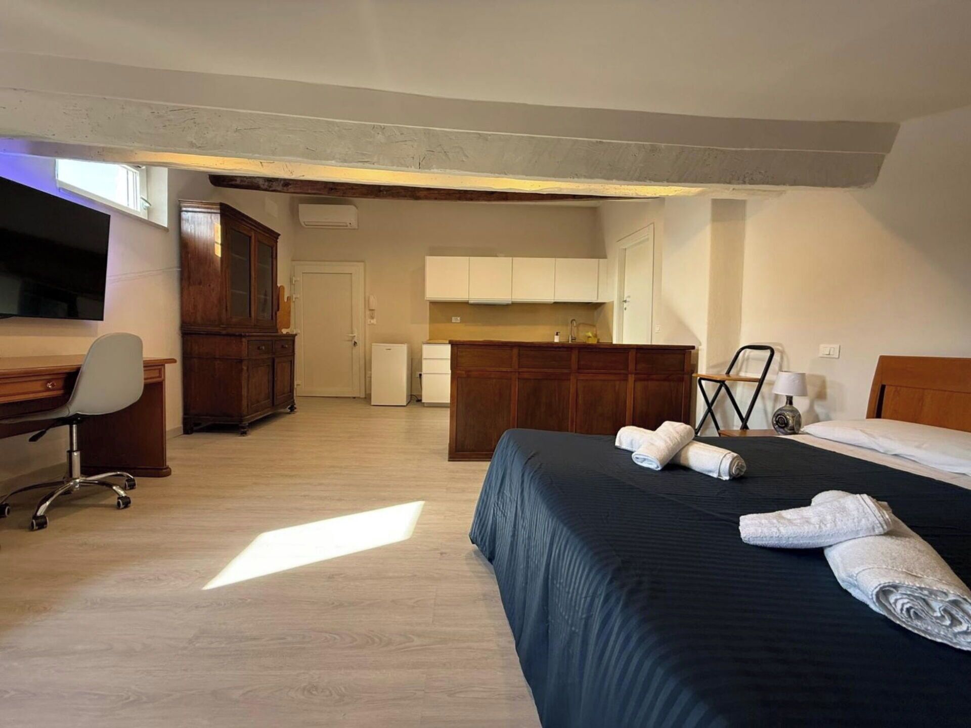 A hotel room with a bed, a desk, a chair, a wardrobe, and a kitchenette.