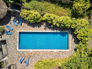 Vista aérea de una piscina rectangular rodeada de pavimento de piedra, con varias sillas de descanso y una pequeña mesa.