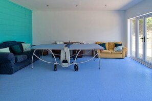 Ein Zimmer mit Tischtennisplatte, einer Couch und einem Fenster.