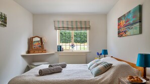 Een slaapkamer met een bed, een raam met uitzicht, een nachtkastje, een lamp en een schilderij aan de muur.