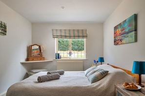 Ein Schlafzimmer mit einem Bett, einem Fenster mit Blick, einem Nachttisch, einer Lampe und einem Bild an der Wand.