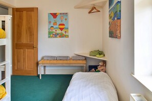 Ein Kinderzimmer mit einem Bett, einer Sitzbank, einem Regal mit Spielzeug und einer Tür.