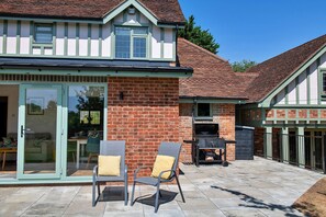 Ein zweistöckiges Haus mit Ziegelaußenwand, einer Terrasse mit zwei Stühlen und einem Grillplatz.