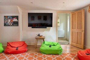 A living room with a flat-screen TV mounted on the wall, a small wooden table with a toy, and two bean bags. - Chillstone House (Rowde)