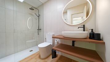 A modern bathroom with a glass shower enclosure, a white toilet, a sink with a round mirror, and a wooden vanity.