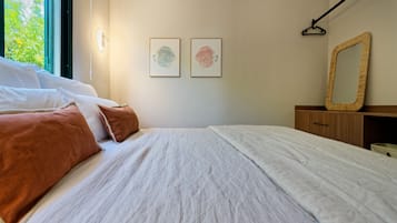 Ett sovrum med en säng, kuddar, ett sängbord, en spegel och två inramade konstverk på väggen.