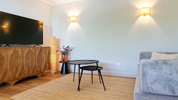 Ett modernt vardagsrum med en platt-TV, ett träskåp, ett runt bord med två stolar och en soffa.